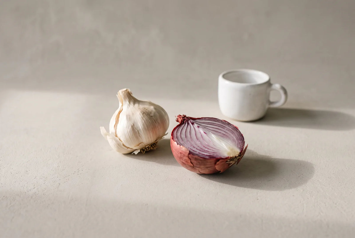 Gousses d'ail, oignon, tasse de café et pomme posés sur une table de cuisine