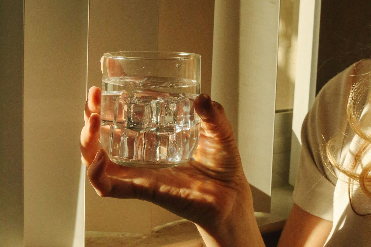 Une main tient un verre d'eau à contre-jour, dans la lumière du matin