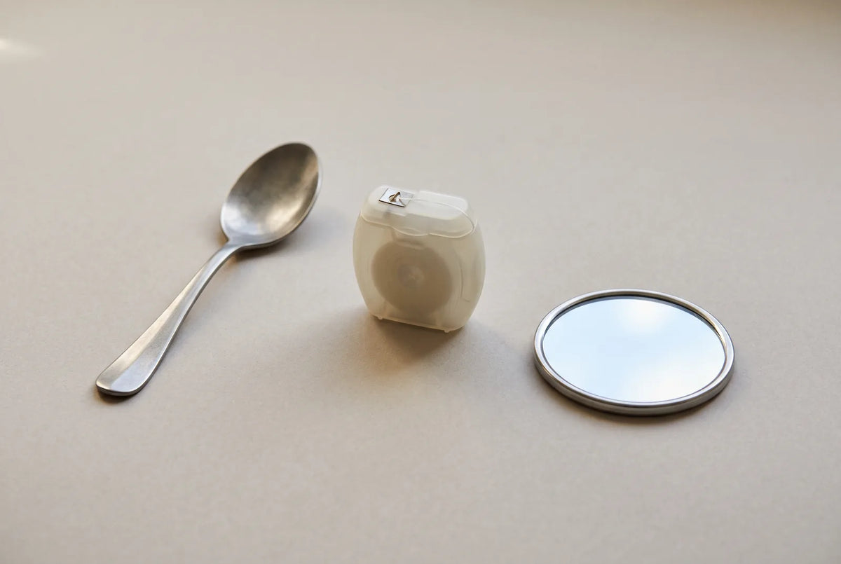 Une cuillère en plastique posée près d'un fil dentaire et d'un verre d'eau sur un plan de salle de bains